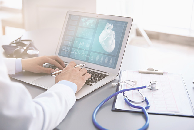 ノートパソコンの画面に映る心臓画像や心電図を確認する医師の手元